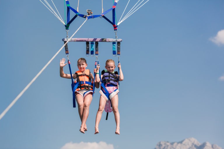 Two happy girls parasailing - one waving